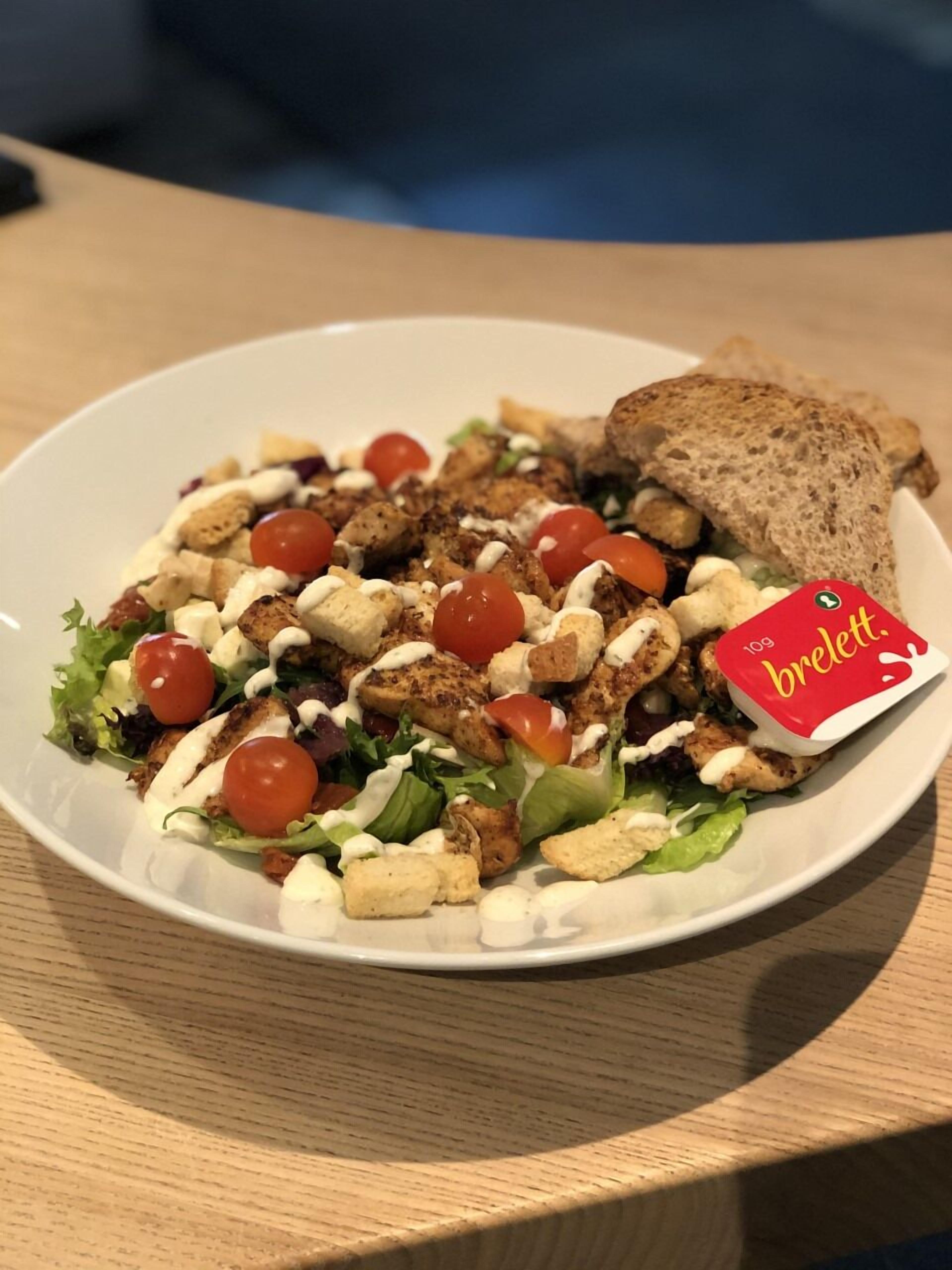 A plate of food with a salad, grilled chicken, and a slice of bread.