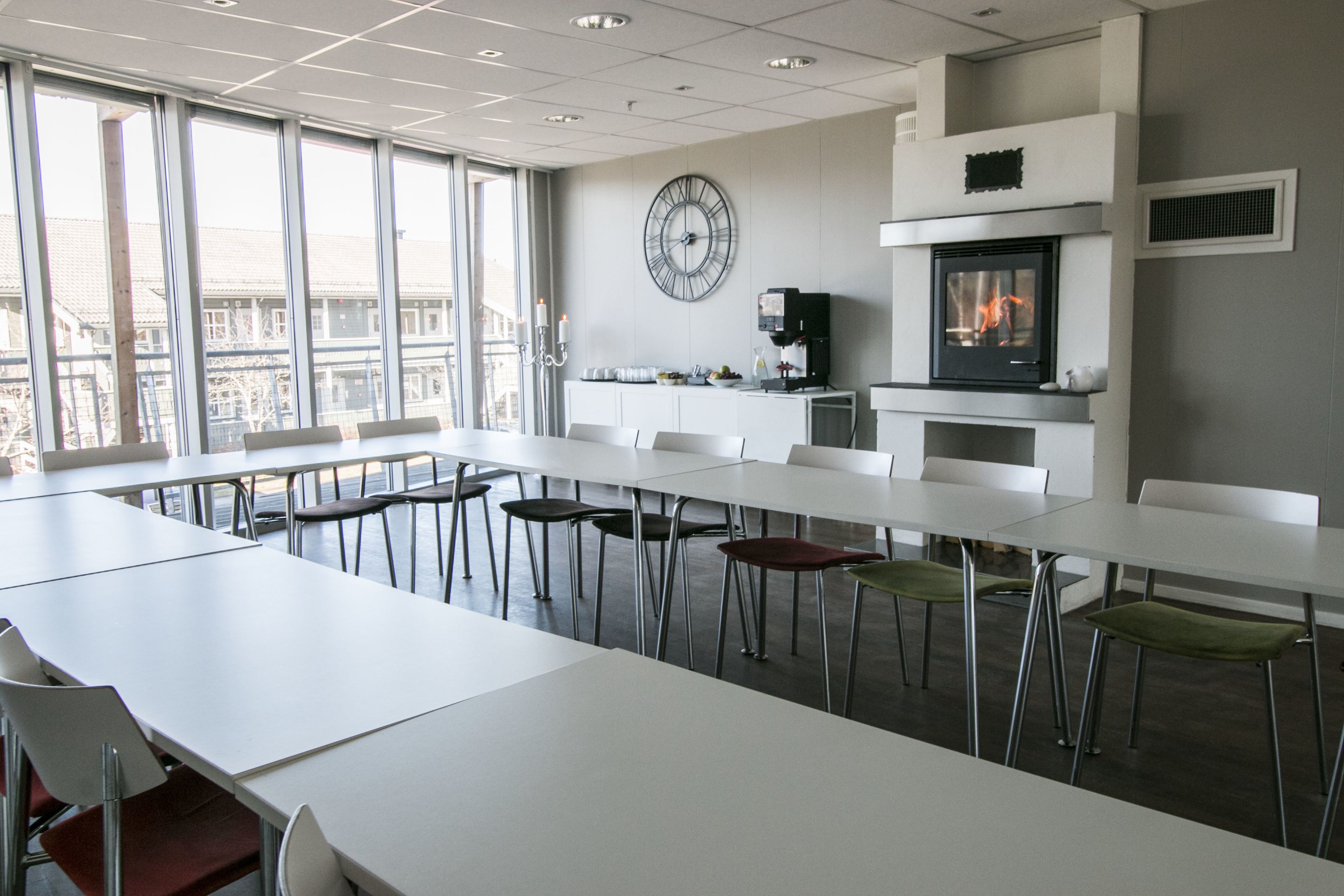 A modern conference room with white tables and chairs, a large wall clock, and a fireplace.