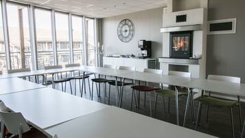 Una sala de conferencias moderna con mesas y sillas blancas, un reloj de pared grande y una chimenea.