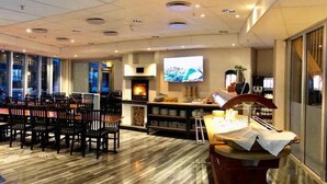 A spacious room with a fireplace, a television mounted on the wall, and a bar area with a counter and stools. - Vikingskipet Hamar Hostel & Apartments (Hamar)