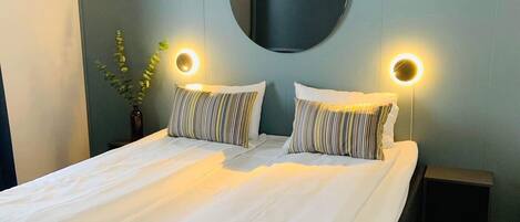 Un dormitorio moderno con una cama grande, dos mesitas de noche, un espejo redondo e iluminación empotrada.