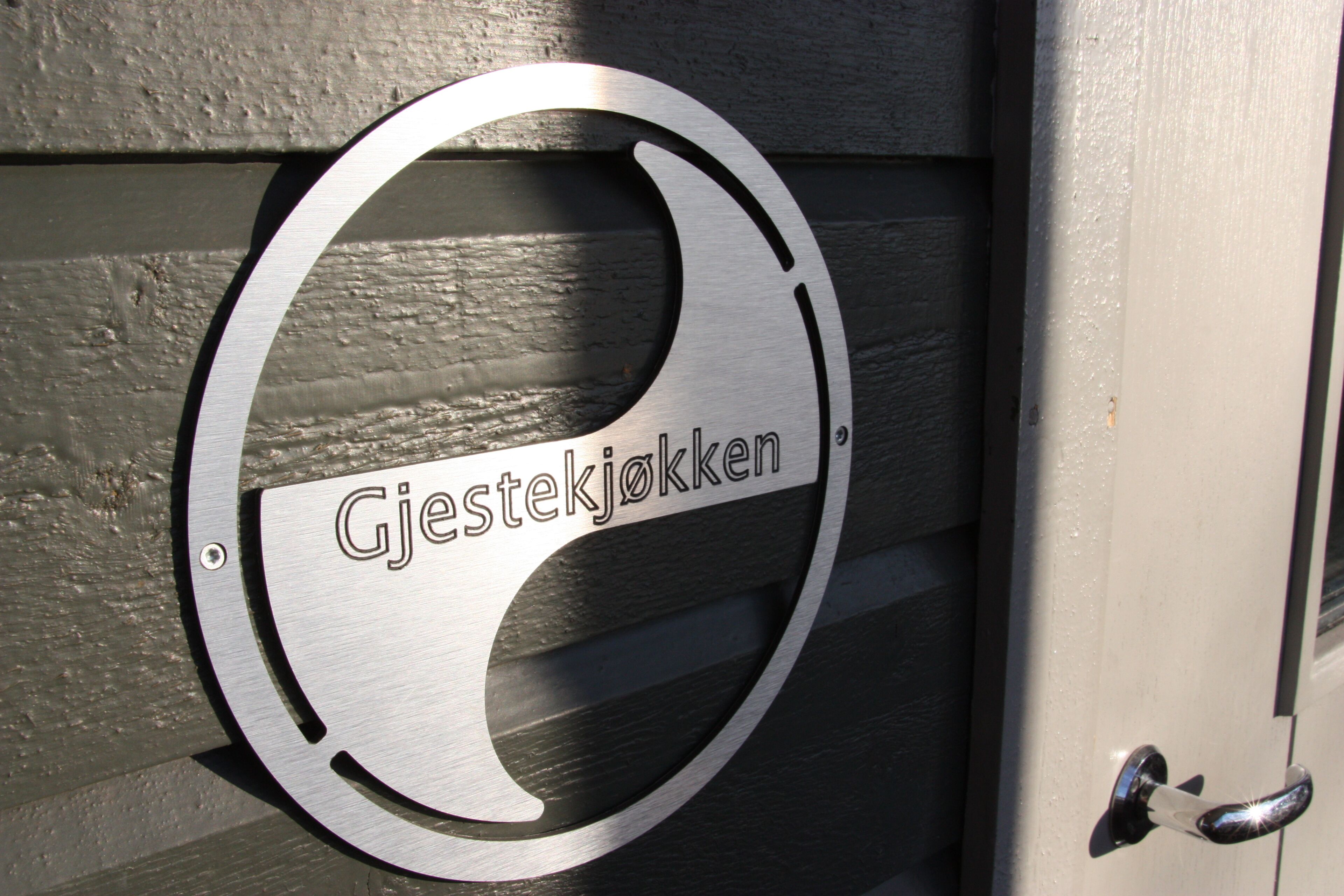 Un letrero metálico con la inscripción 'Gjestekjokken' en una puerta de madera.