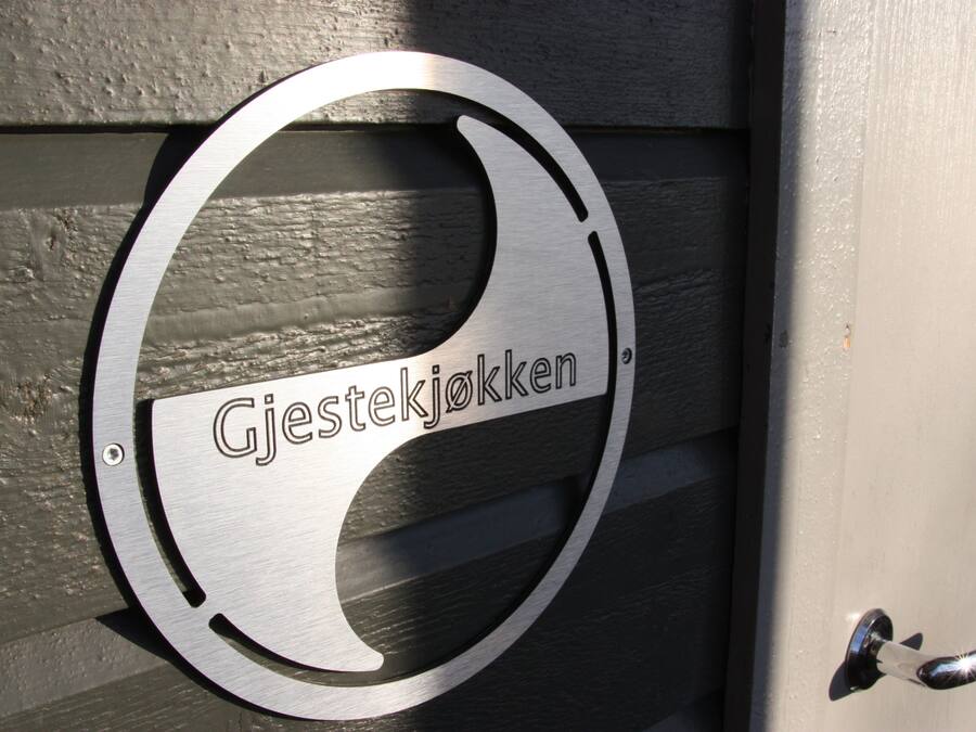 Un letrero metálico con la inscripción 'Gjestekjokken' en una puerta de madera.
