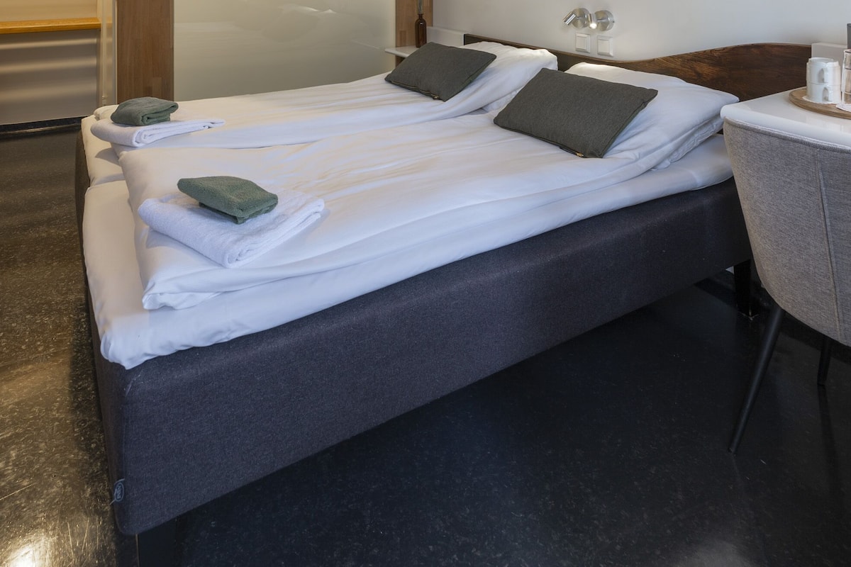 A modern hotel room with a large bed, a small desk, and a mirror.