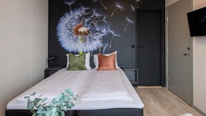 A modern hotel room with a bed, a small table with a plant, a white armchair, and a wall-mounted TV. - Vikingskipet Hamar Hostel & Apartments (Hamar)