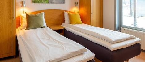 Quarto de hotel com duas camas, um guarda-roupa de madeira, um quadro e uma janela com vista.