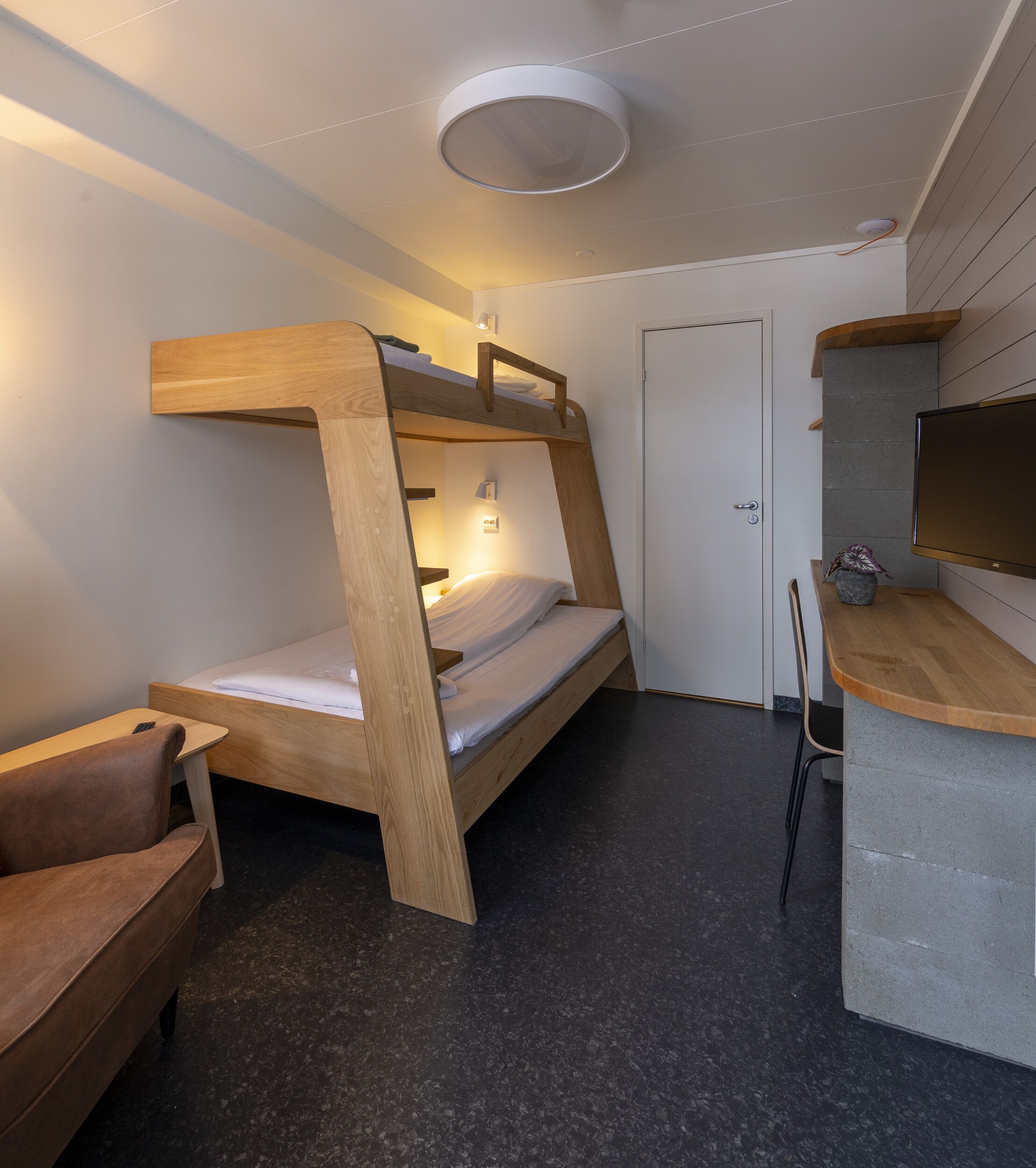 A compact room with a bunk bed, a desk, a chair, and a television.