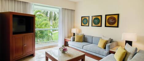 A modern living room with a large flat-screen TV, a grey sofa, a coffee table with a vase, and a balcony with curtains.
