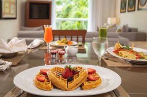 Desayuno con waffles, fruta y bebidas sobre una mesa.