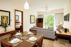 Una habitación bien iluminada con una mesa de comedor preparada para cuatro, un sofá, un televisor y un ventanal con vistas a zonas verdes.