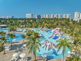 Un parque acuático con toboganes y piscinas, rodeado de palmeras y edificios de hotel al fondo.