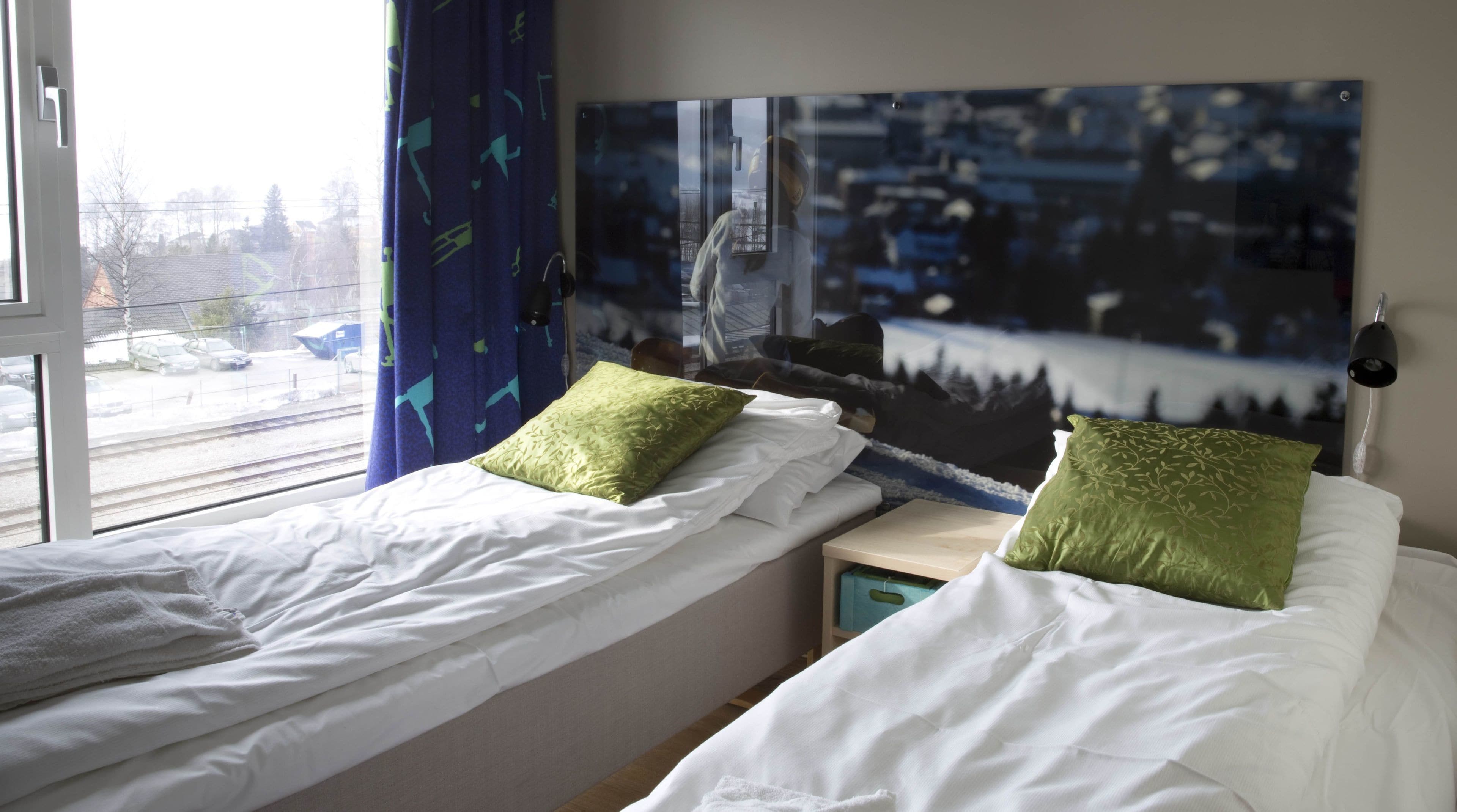 Et hotelværelse med to senge, et stort vindue med udsigt til tog og biler, og et bybillede som billedkunst på væggen.