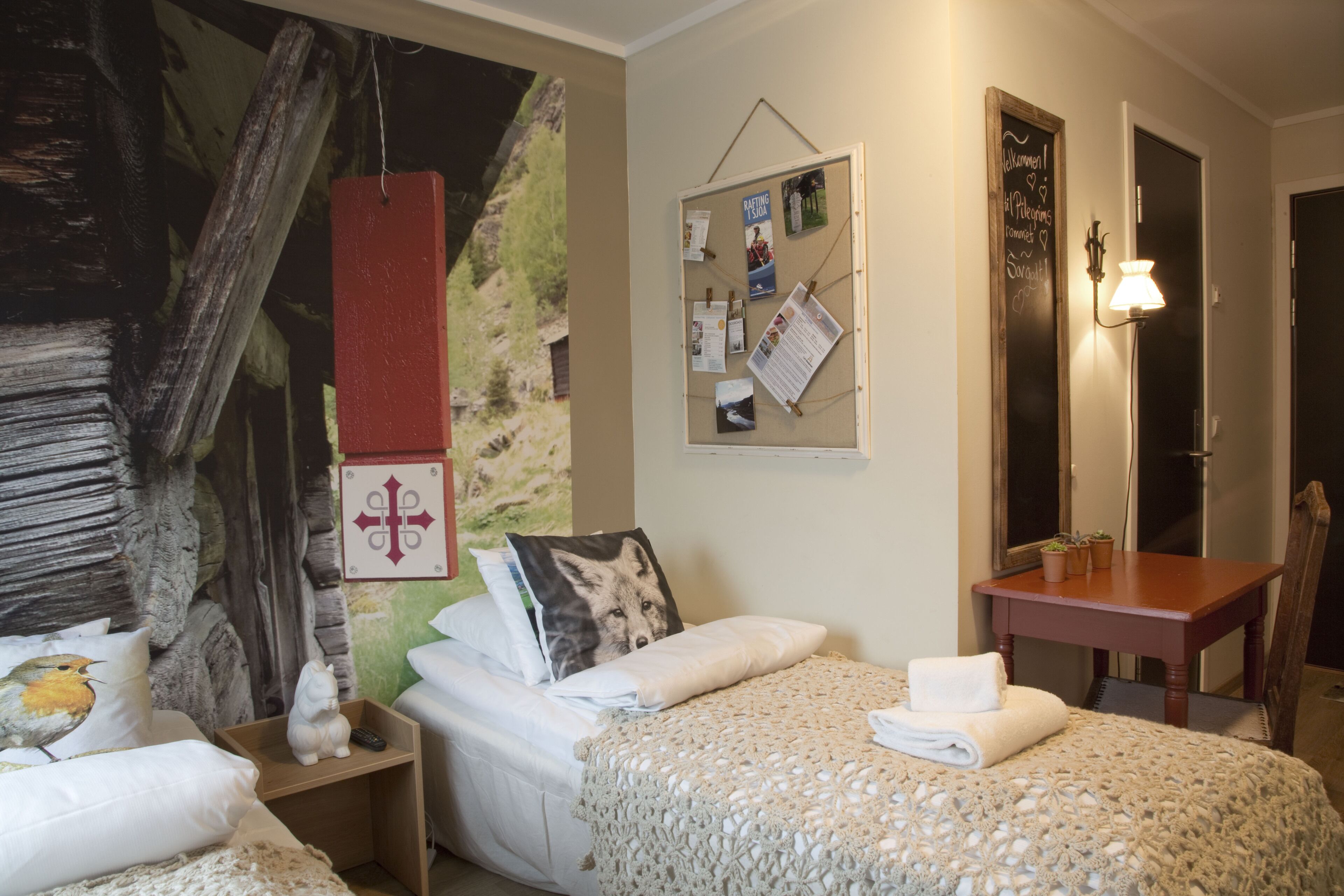 Una camera da letto con un letto, un comodino, una bacheca a parete, una sedia di legno e un piccolo tavolo con una lampada.