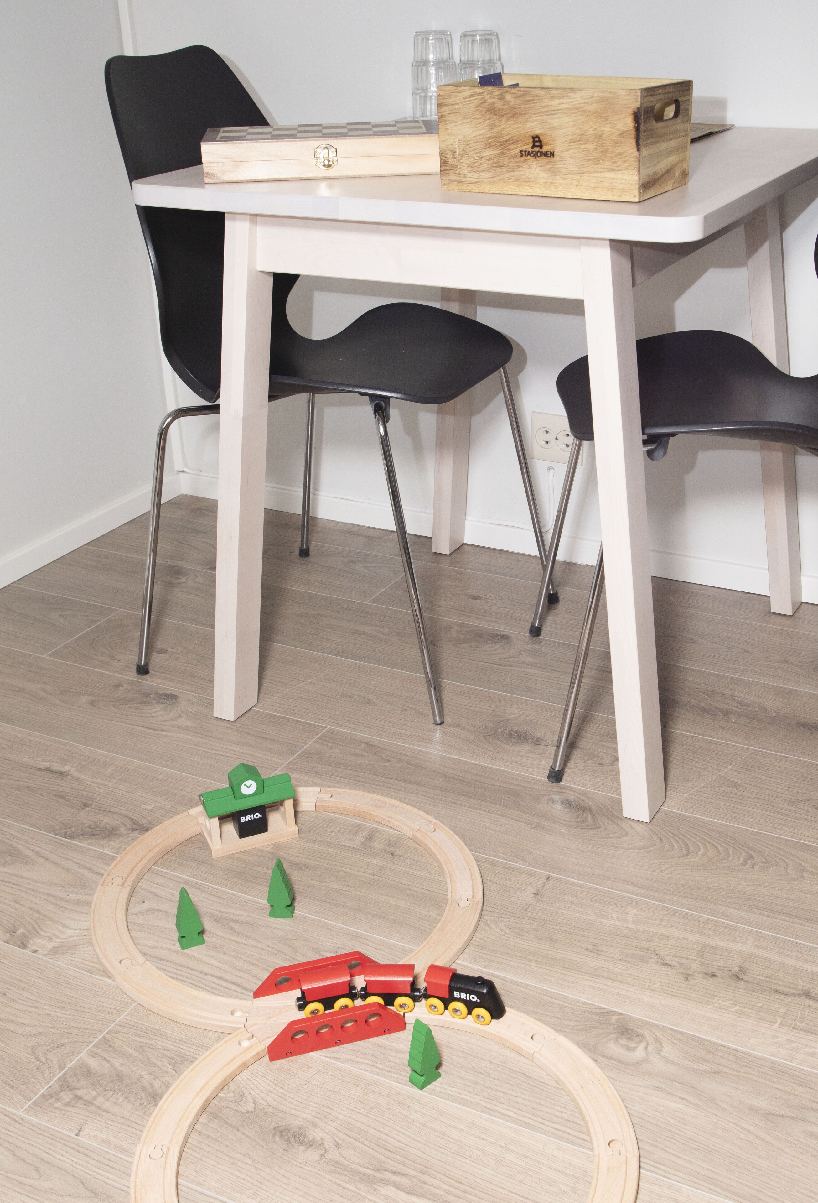 A room with a wooden table, black chairs, and a toy train set on the floor.