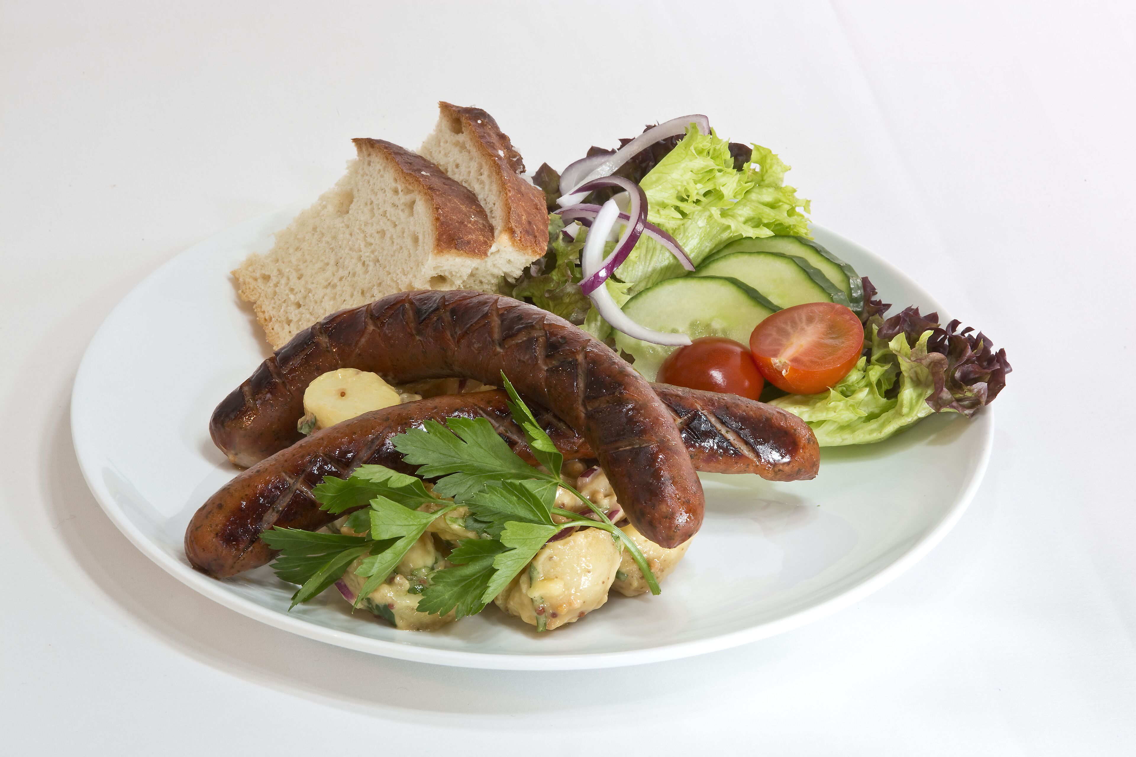 Un piatto con salsicce alla griglia, una fetta di pane e un'insalata come contorno.