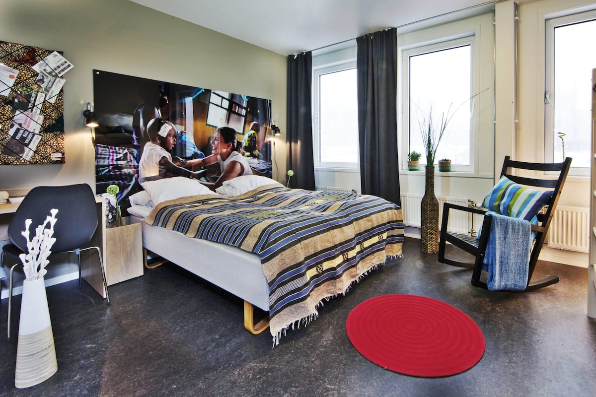 Quarto moderno com uma cama grande, um tapete vermelho, uma cadeira e uma televisão na parede.