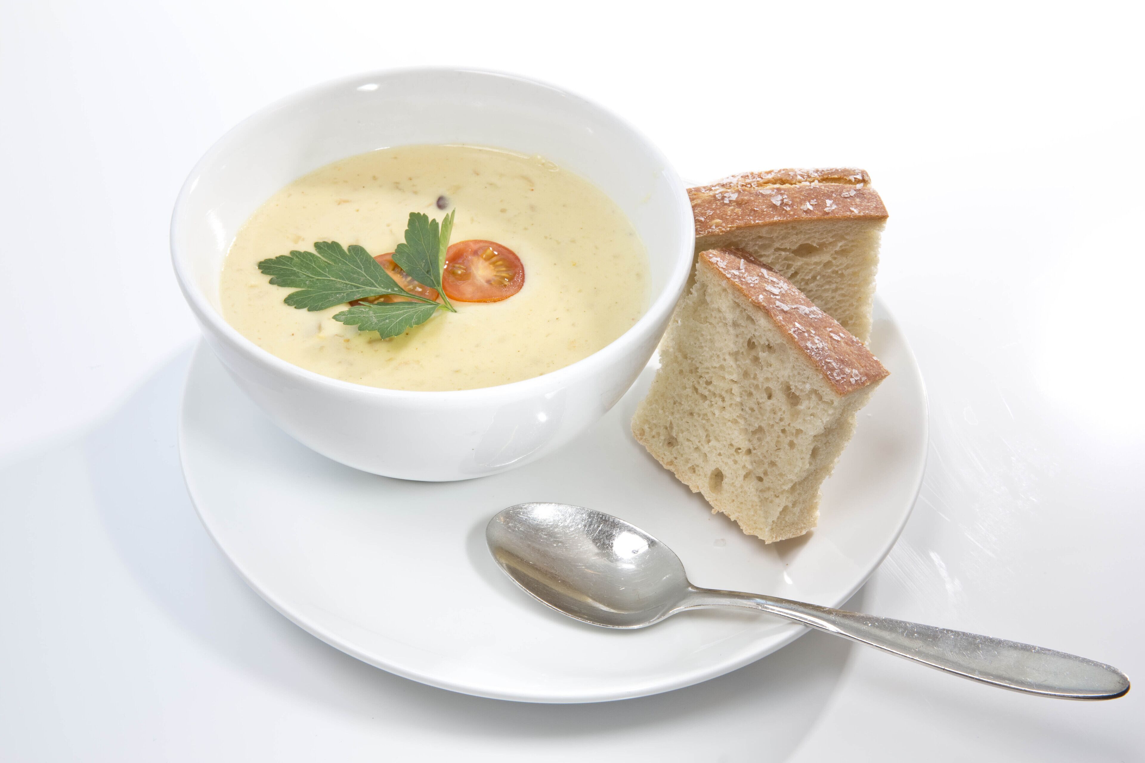 Un tazón de sopa con decoración, acompañado de una rebanada de pan y una cuchara sobre un plato blanco.