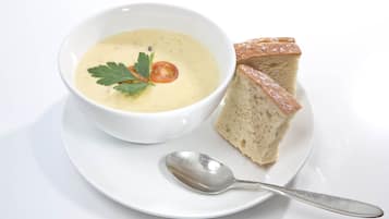 Un tazón de sopa con decoración, acompañado de una rebanada de pan y una cuchara sobre un plato blanco.