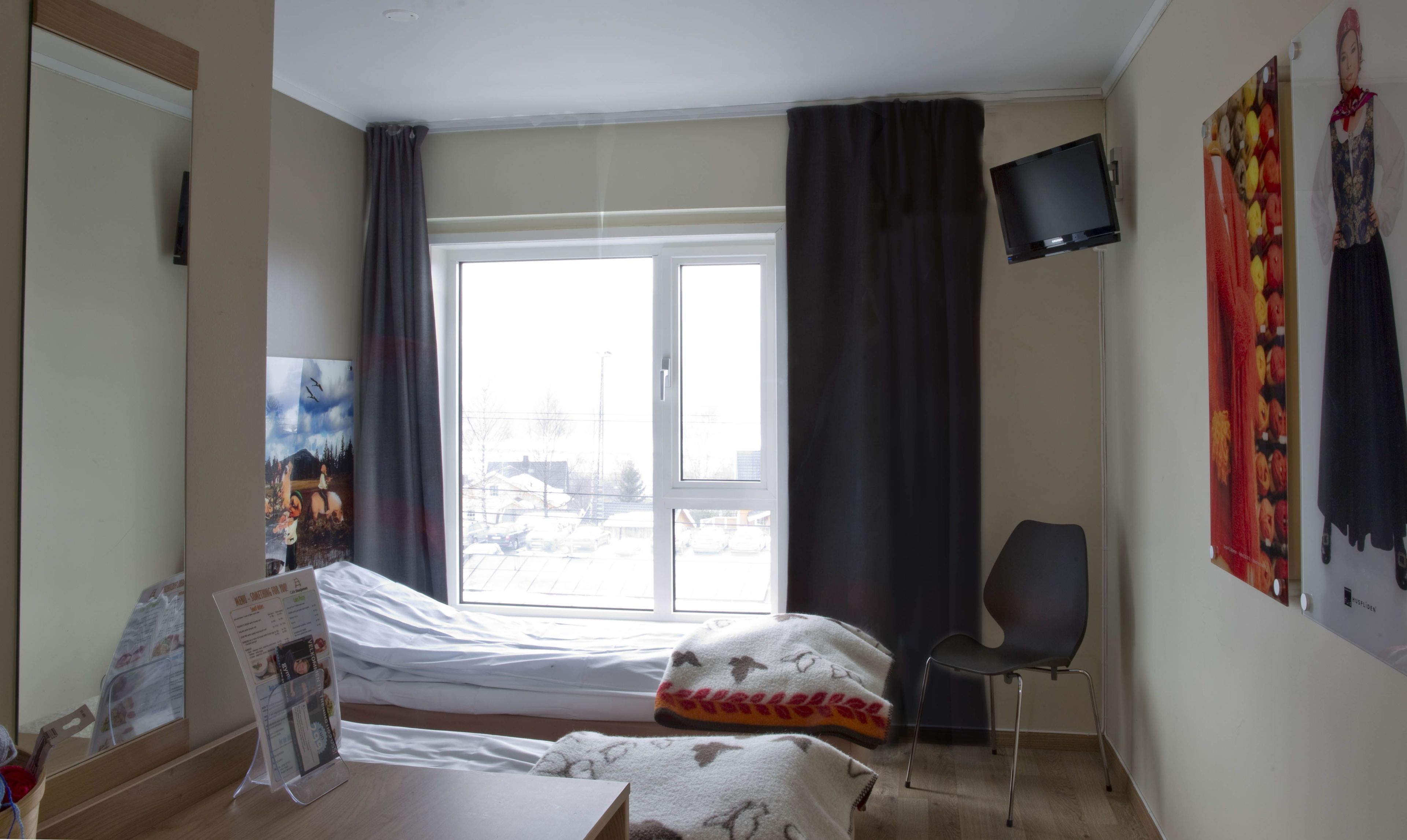 A hotel room with a bed, a chair, a TV, and a window with curtains.