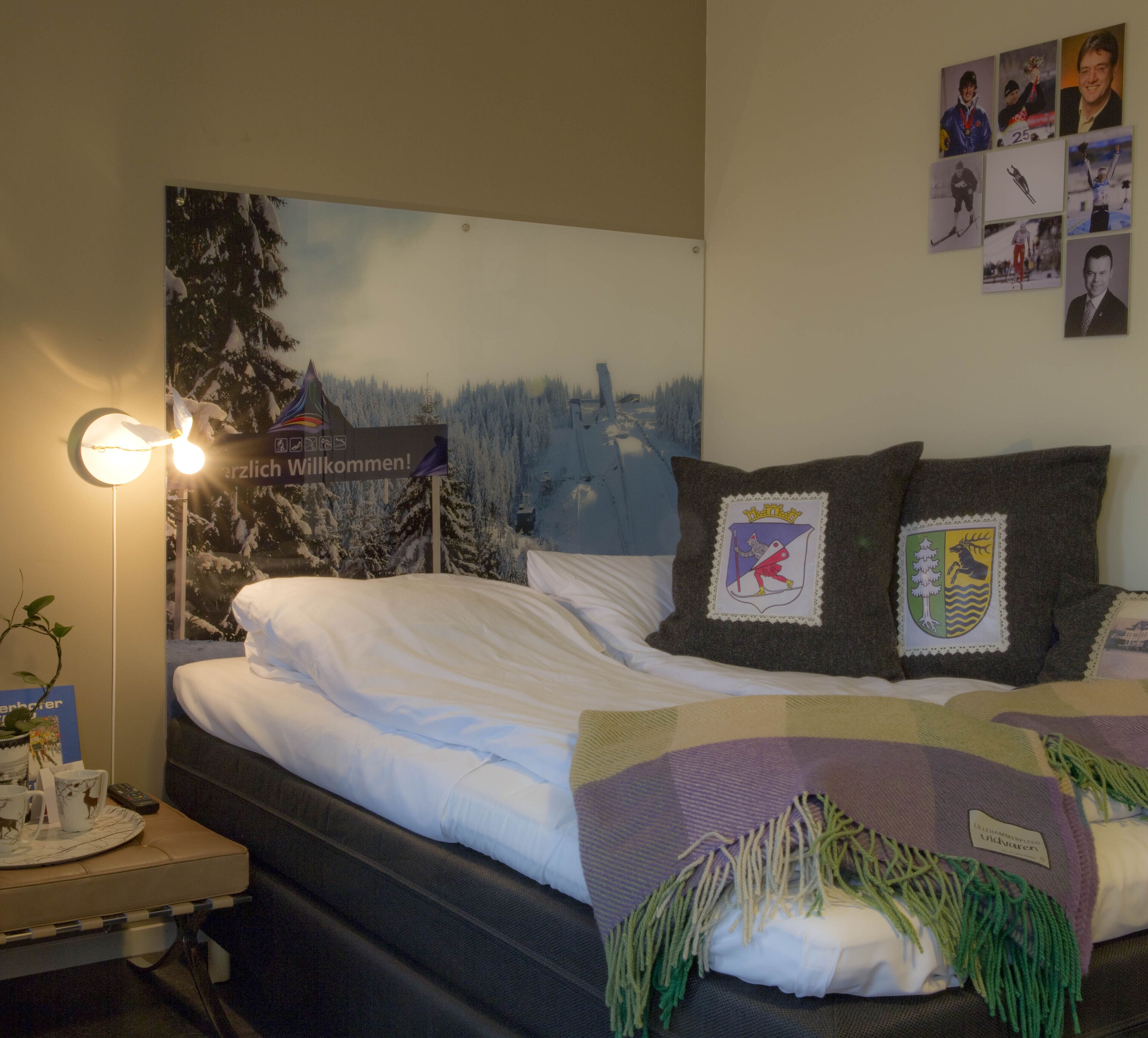 A hotel room with a bed, a nightstand with a lamp, and a poster on the wall.