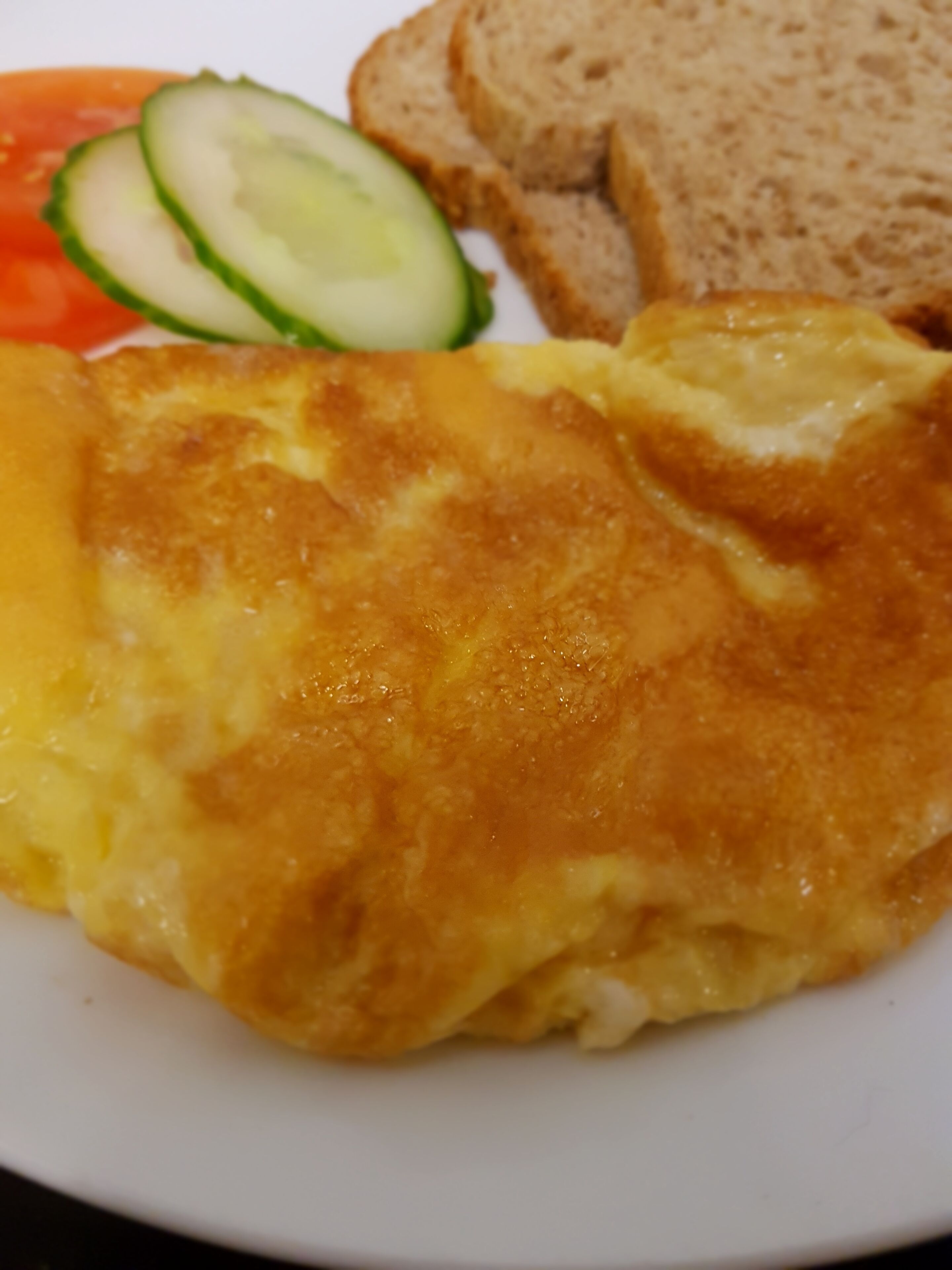 Une assiette contenant une omelette, des tranches de pain et des légumes coupés en tranches.