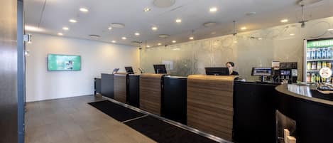 Un área de recepción con diseño moderno, que incluye un mostrador de recepción, una pantalla digital y un dispensador de bebidas.