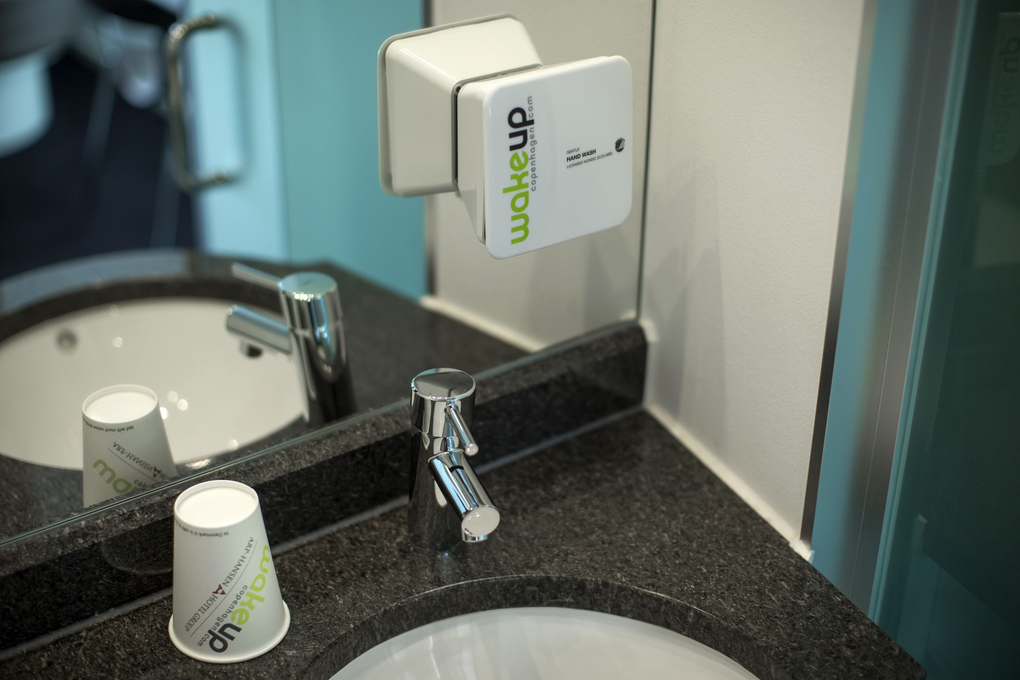 A bathroom sink with a hand soap dispenser and a cup.