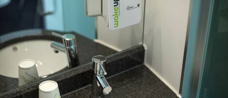 A bathroom sink with a hand soap dispenser and a cup.