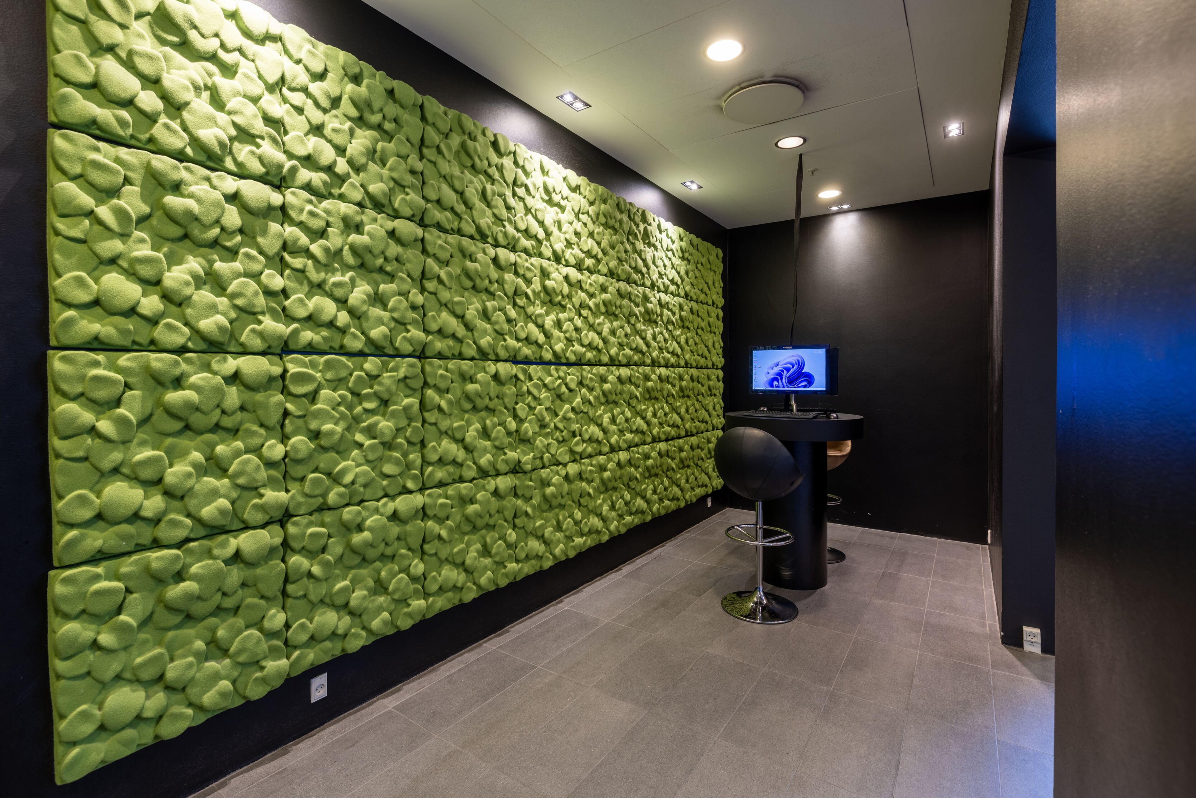 A modern interior with a green acoustic panel wall, a reception desk, and a bar area.