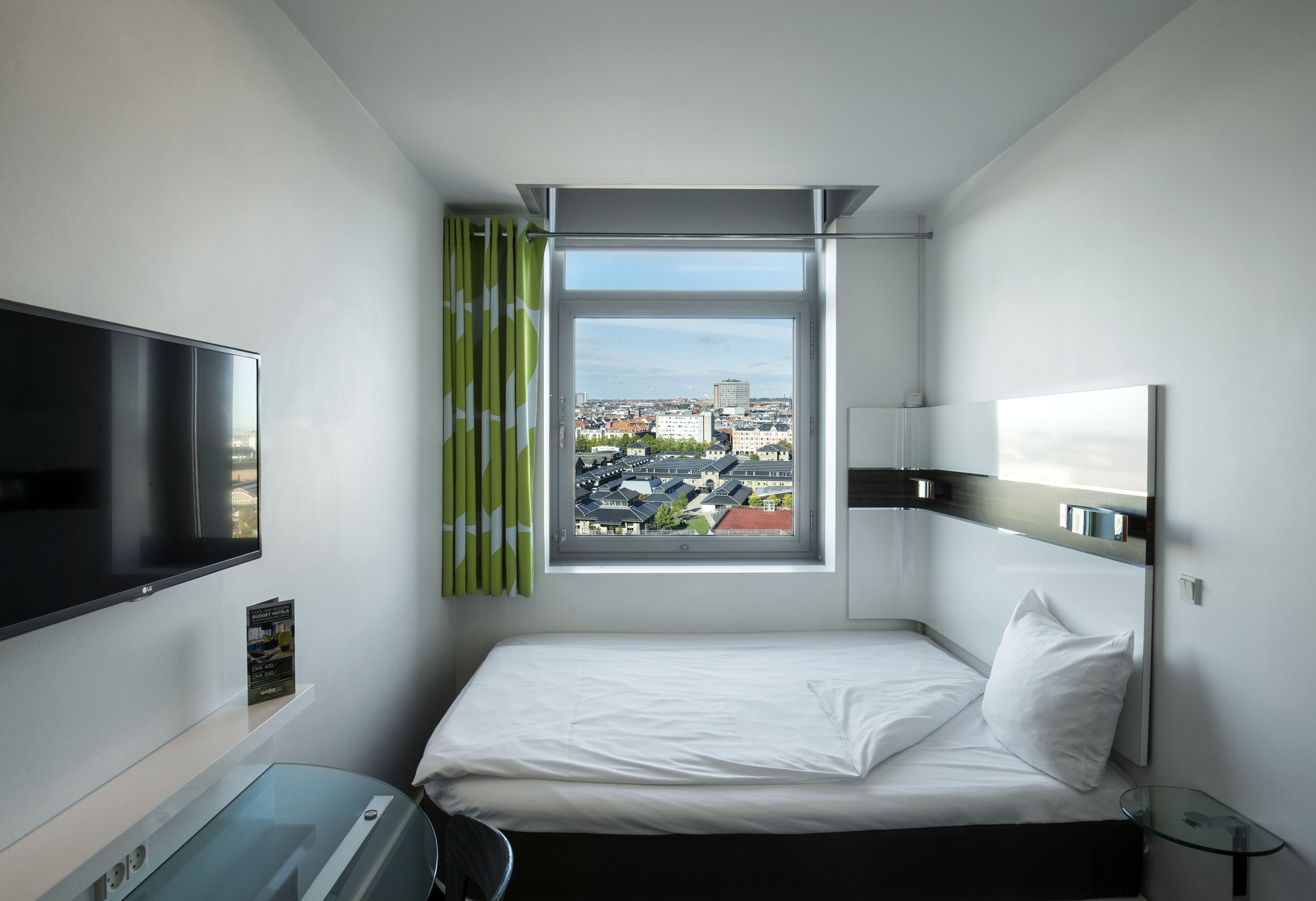 A hotel room with a bed, a TV, a window with curtains, and a city view.