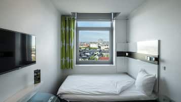 Habitación de hotel con cama, televisor, ventana con cortinas y vista a la ciudad.