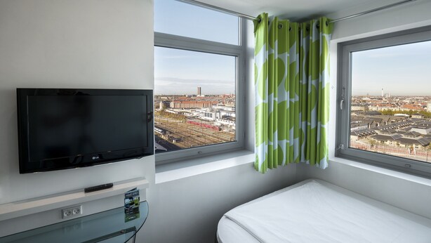 Habitación de hotel con televisión, cama y ventanas amplias con vista a la ciudad.