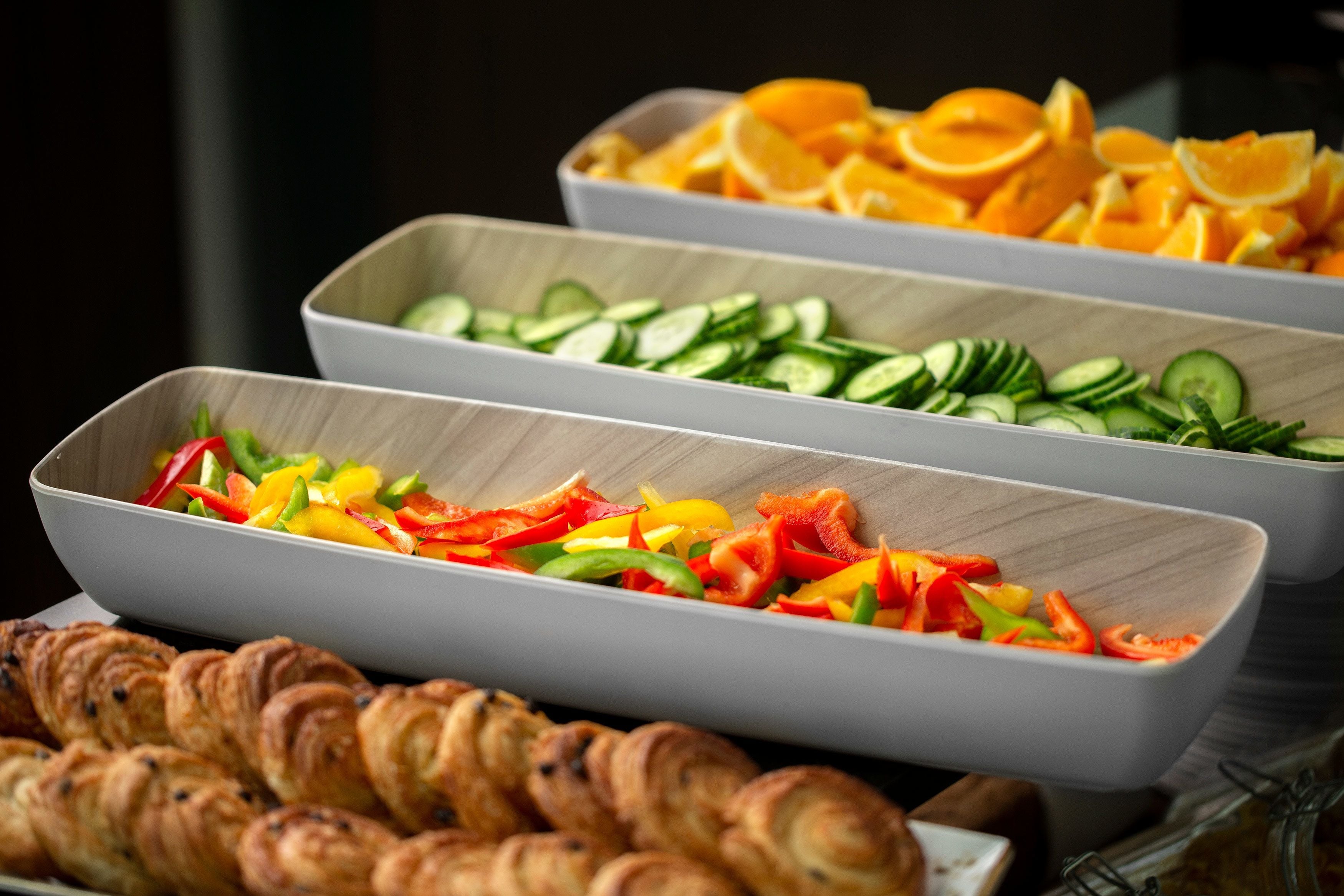 A buffet with various food items including sliced vegetables, fruits, and pastries.