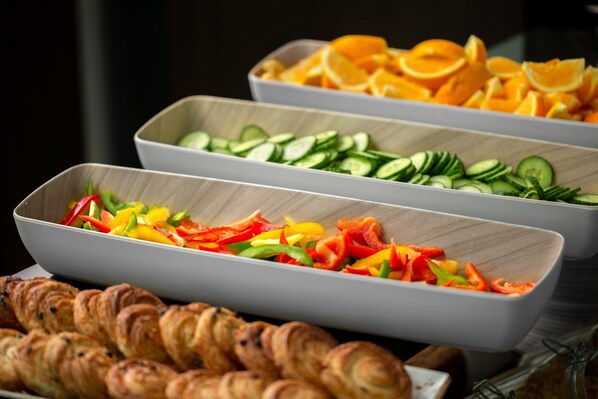 A buffet with various food items including sliced vegetables, fruits, and pastries.