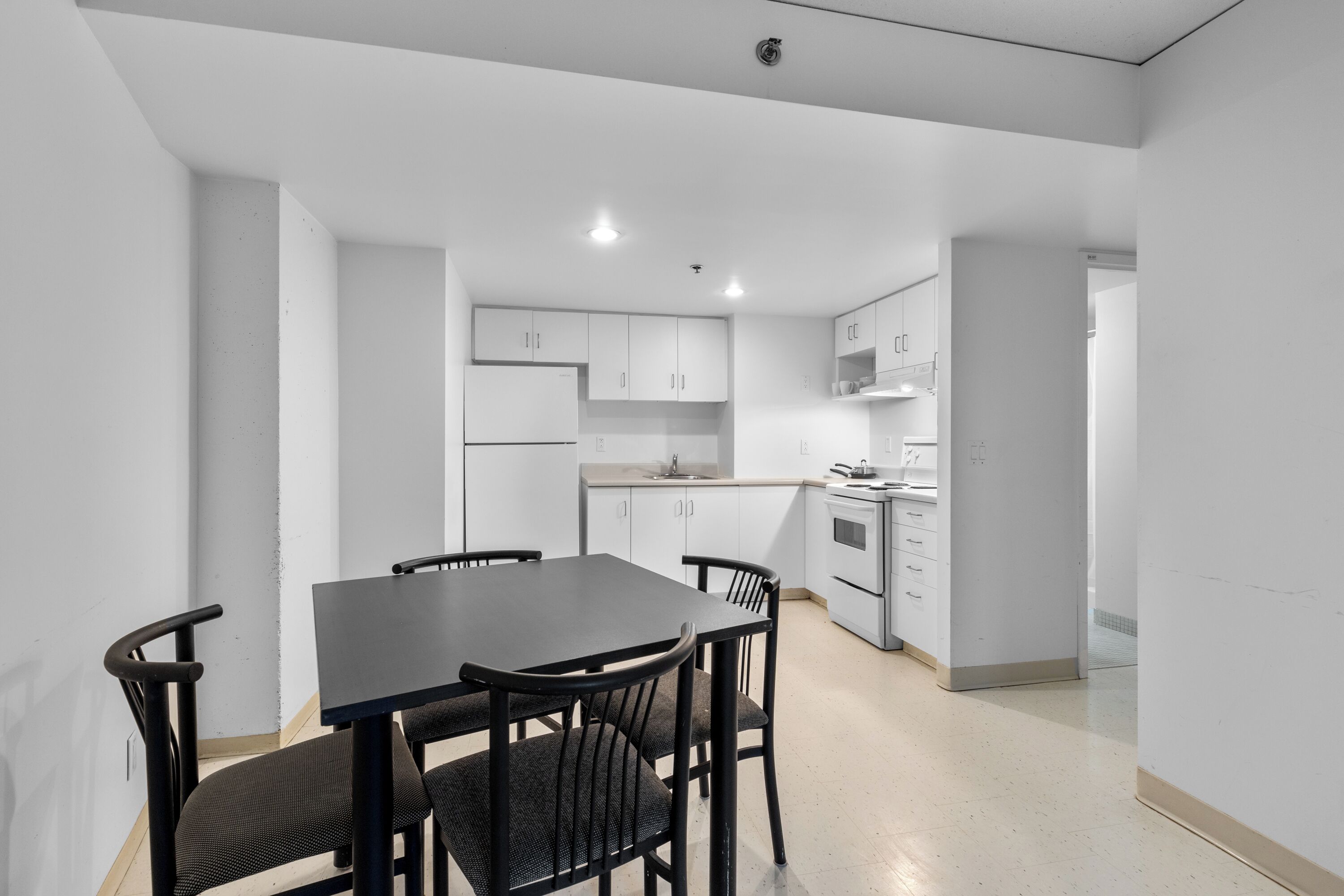 A modern kitchen with white cabinets, a black dining table, and four chairs.