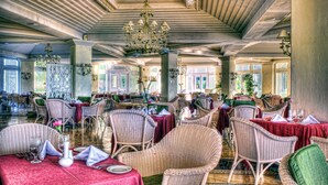 A spacious dining area with wicker chairs and tables, a chandelier, and large windows allowing natural light. - Pueblo Bonito Emerald Luxury Villas & Spa - All Inclusive (Mazatlán)