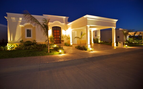 Una propiedad residencial bien iluminada con un camino de entrada cubierto, puerta principal y jardines ajardinados.