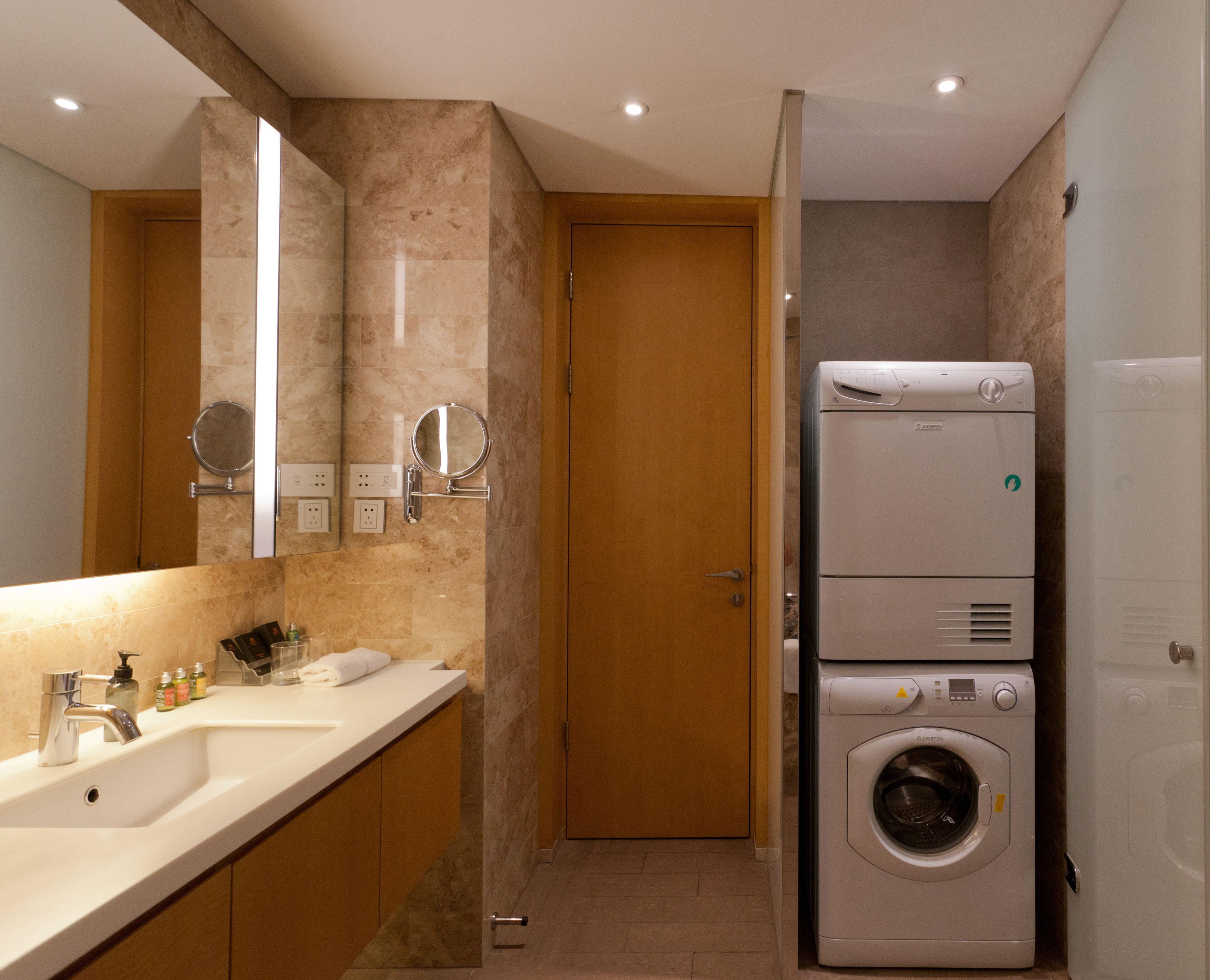 Un baño moderno con lavamanos doble, un espejo, lavadora y una puerta.