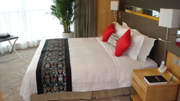 A hotel room with a bed, a bedside table with a phone, a lamp, and a plant.