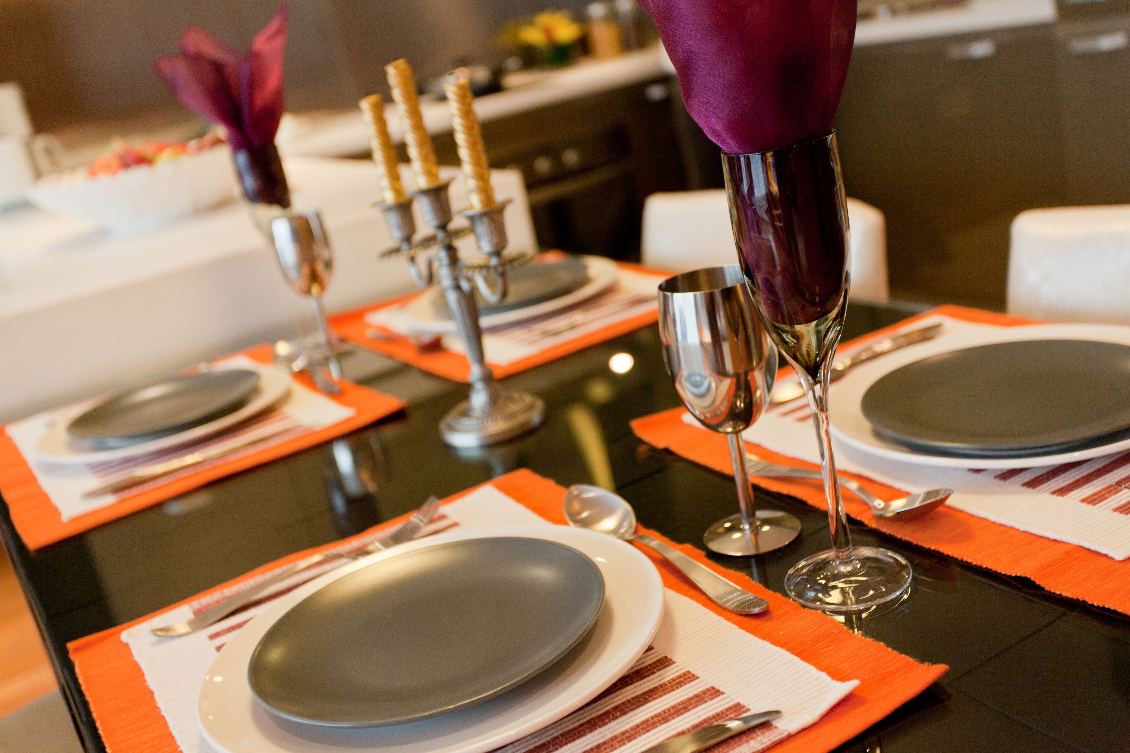 Mesa de comedor dispuesta con platos, cubiertos y velas, lo que sugiere un ambiente de cena formal.