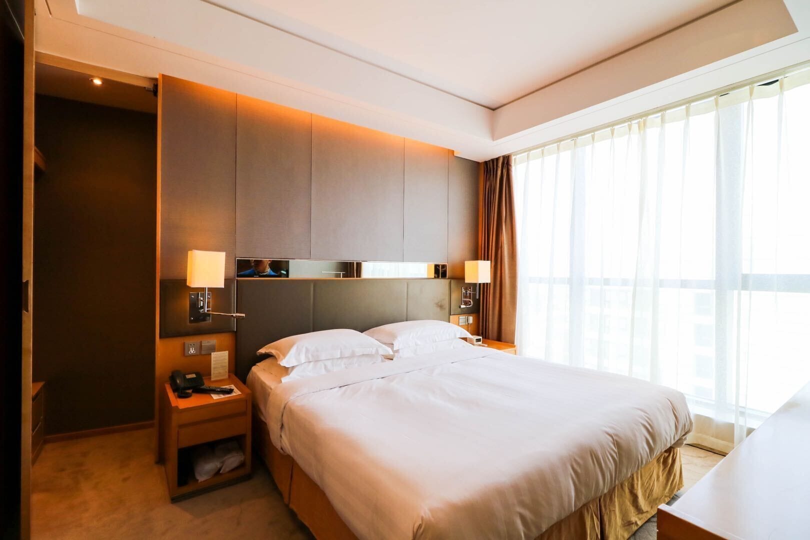 A hotel room with a large bed, bedside tables, a TV, and a window with curtains.