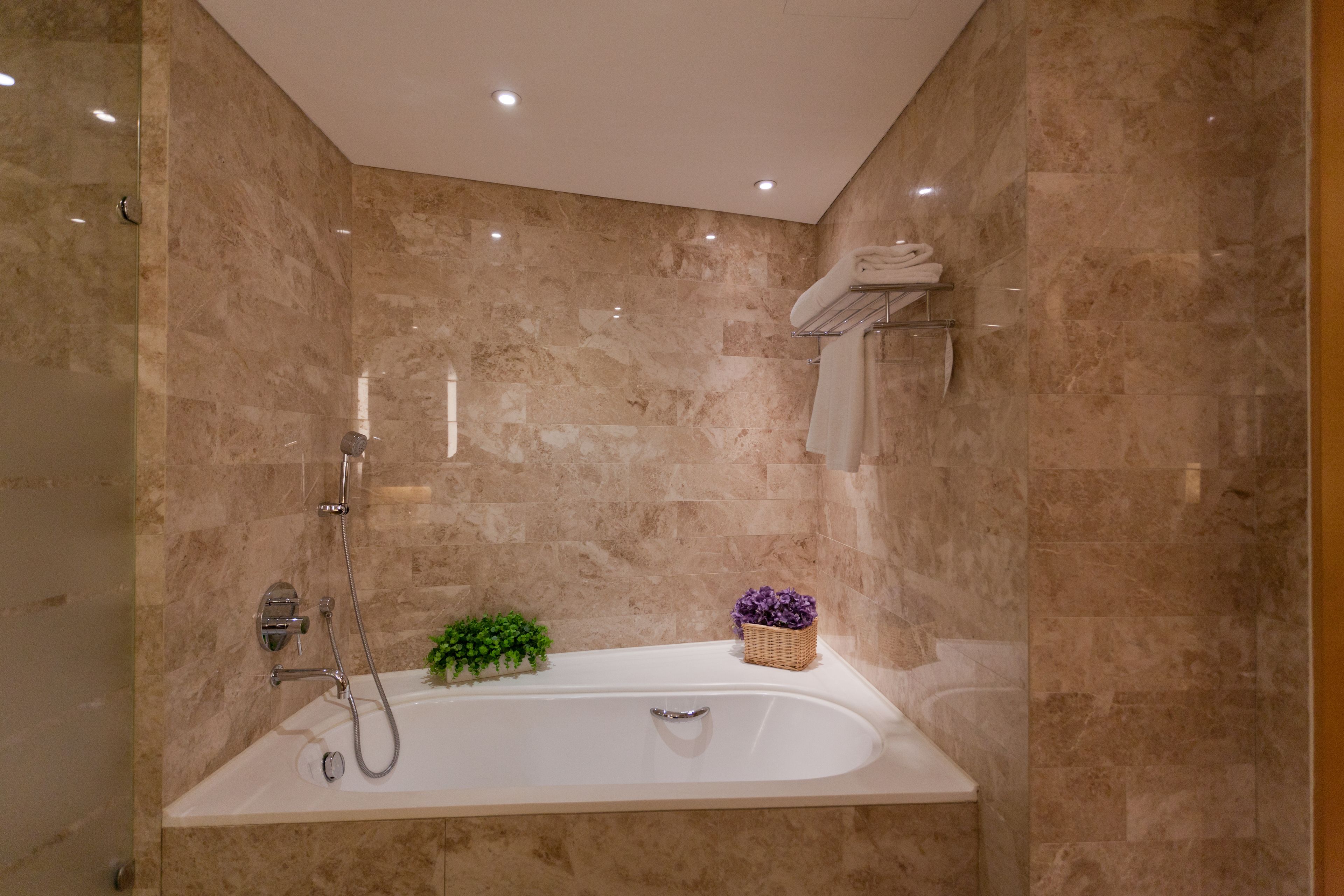 Ein modernes Badezimmer mit einer freistehenden Badewanne, Marmorwänden und einer kleinen Pflanze auf dem Waschtisch.