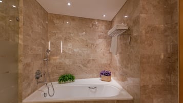 Une salle de bain moderne avec une baignoire sur pieds, des murs en marbre et une petite plante posée sur le meuble-lavabo.