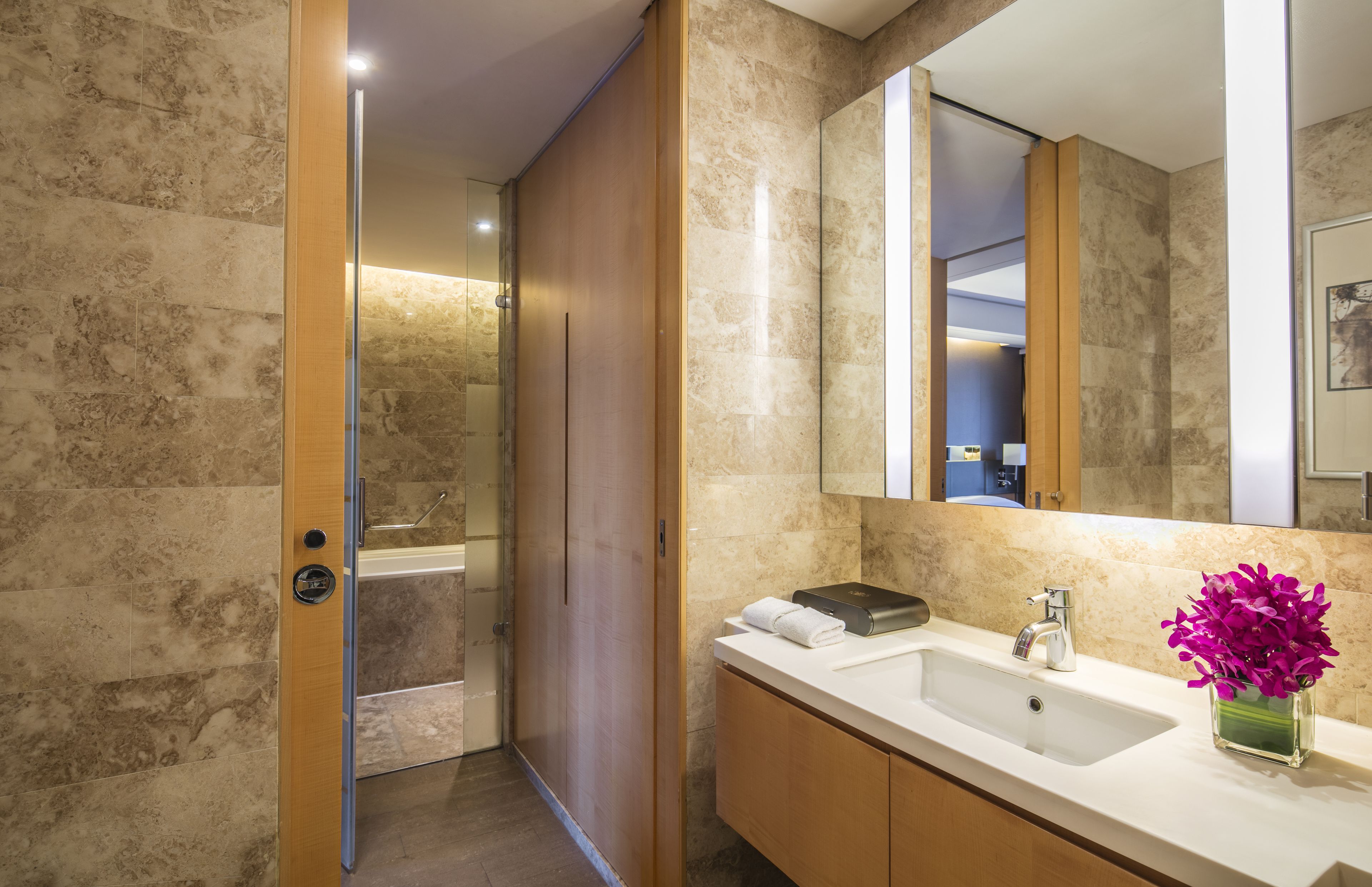 Un baño moderno con pared de mármol, un espejo grande, un lavabo y zona de ducha.