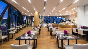 Un restaurante moderno con varias mesas, una zona de bar y amplios ventanales que ofrecen vistas a la ciudad.