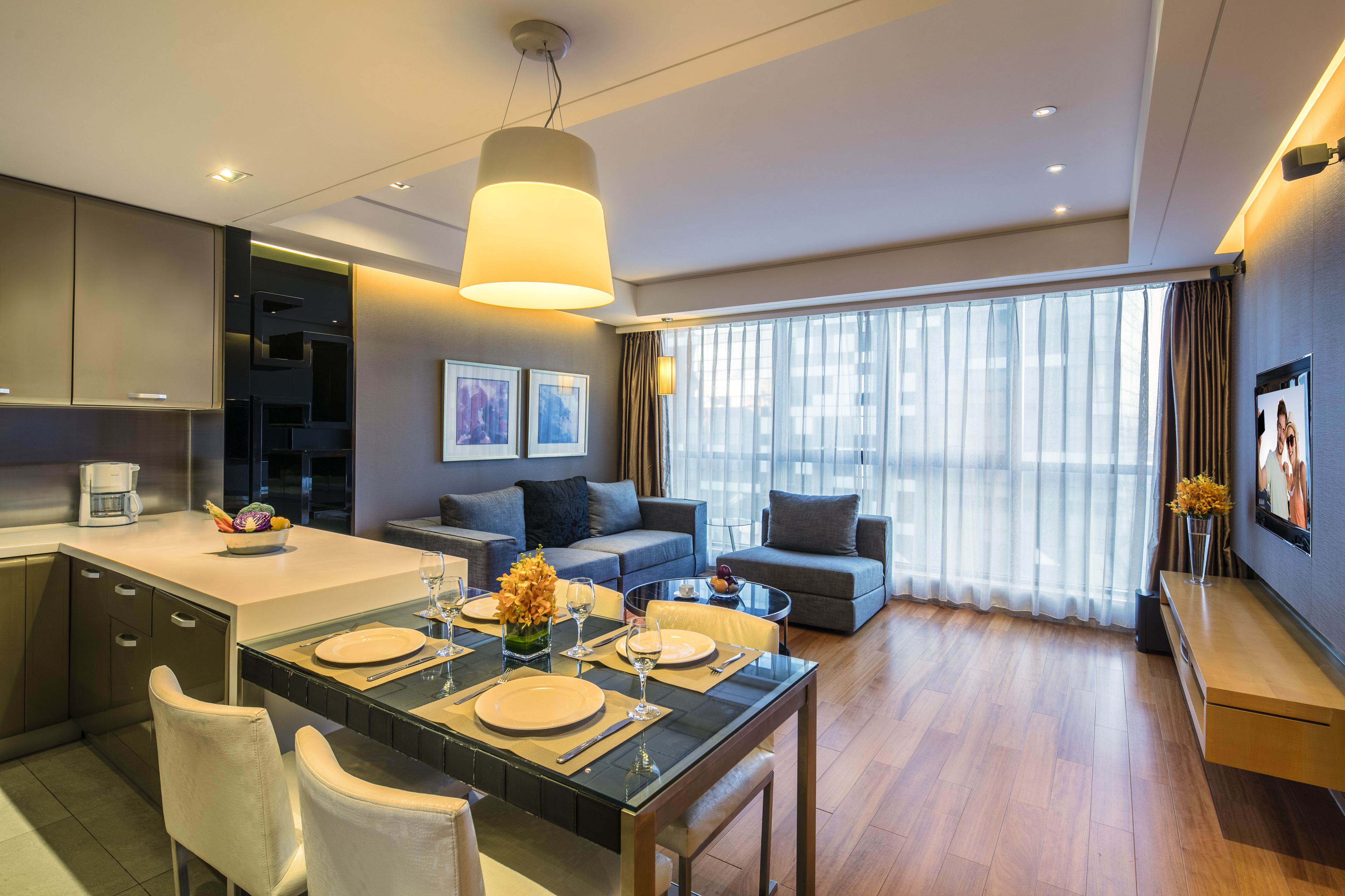 Una habitación de hotel moderna con comedor, sofá, un ventanal con cortinas y un televisor de pantalla plana.