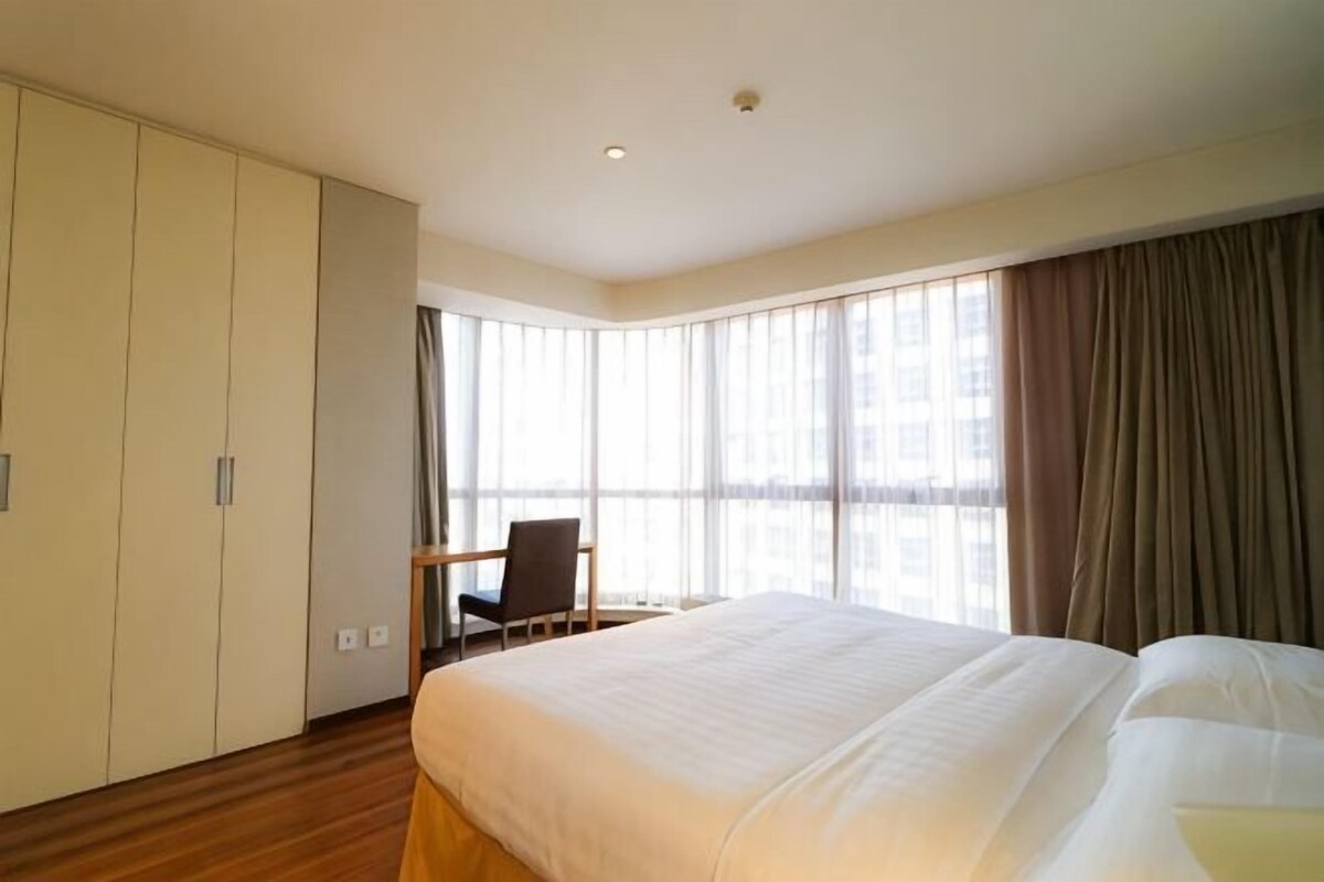 Habitació d'hotel amb un llit gran, una taula de treball i una cadira. Hi ha una finestra amb cortines i el terra és de fusta.