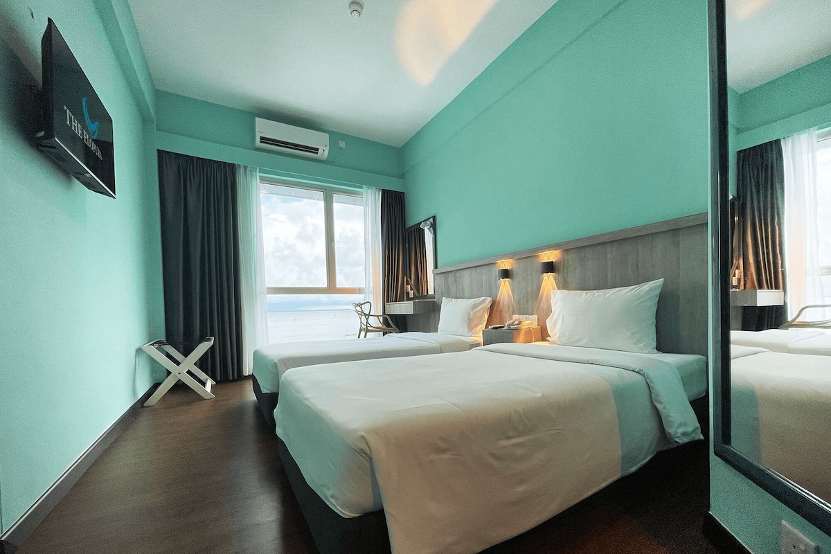 A hotel room with two beds, a large window, an air conditioning unit, and a mirror.