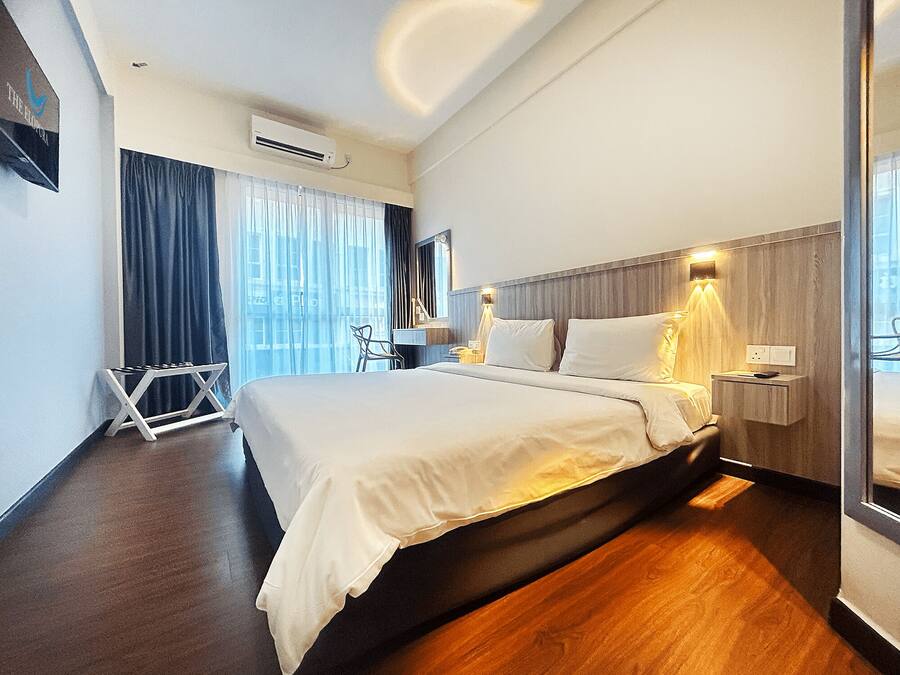 A modern hotel room with a large bed, a wooden floor, a desk with a chair, and a window with curtains.