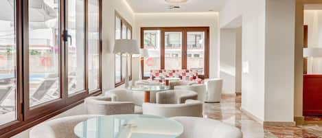 A modern hotel lobby with a glass table, white sofas, and a view of the pool area.